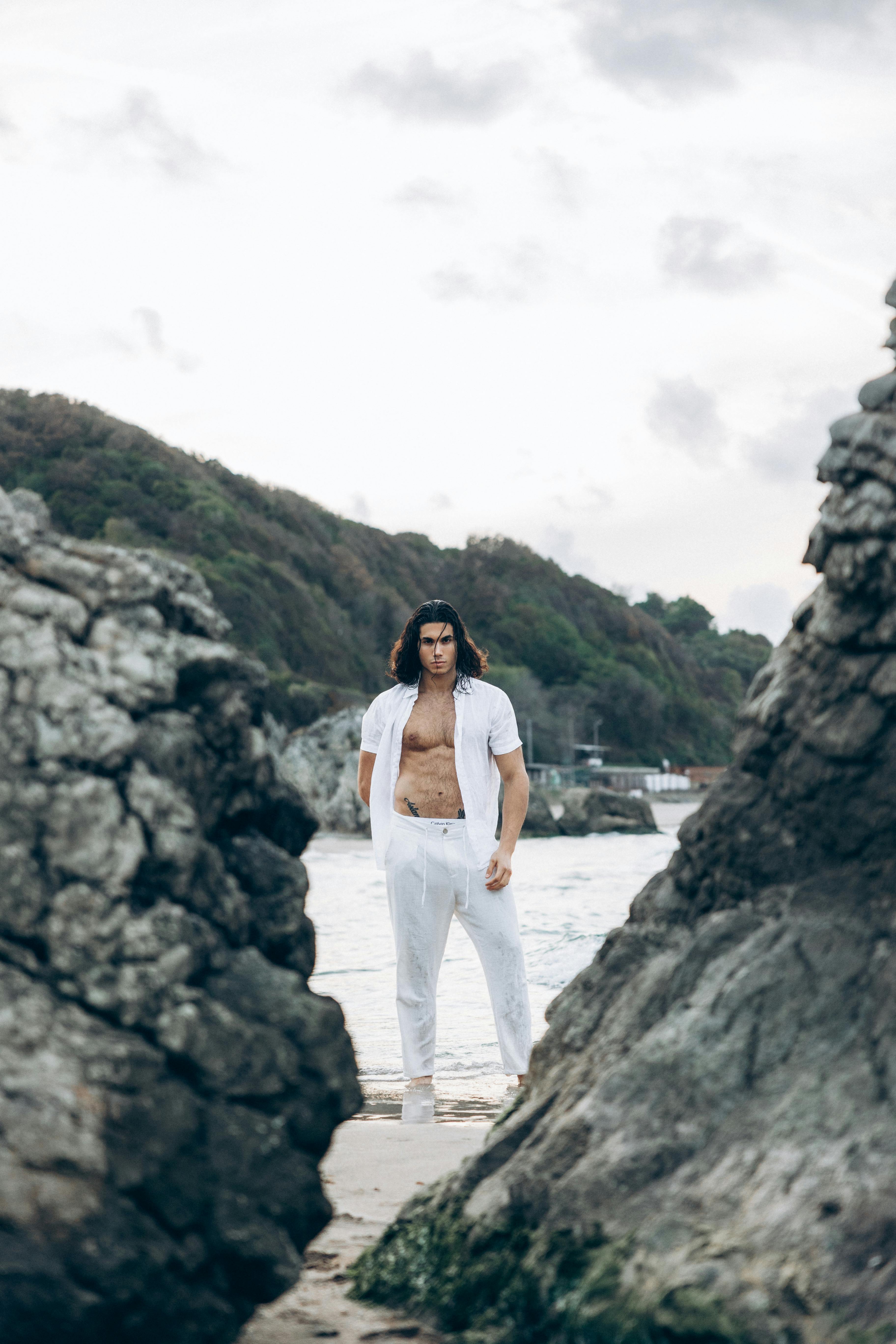 a man in white shirt standing on rocks near water