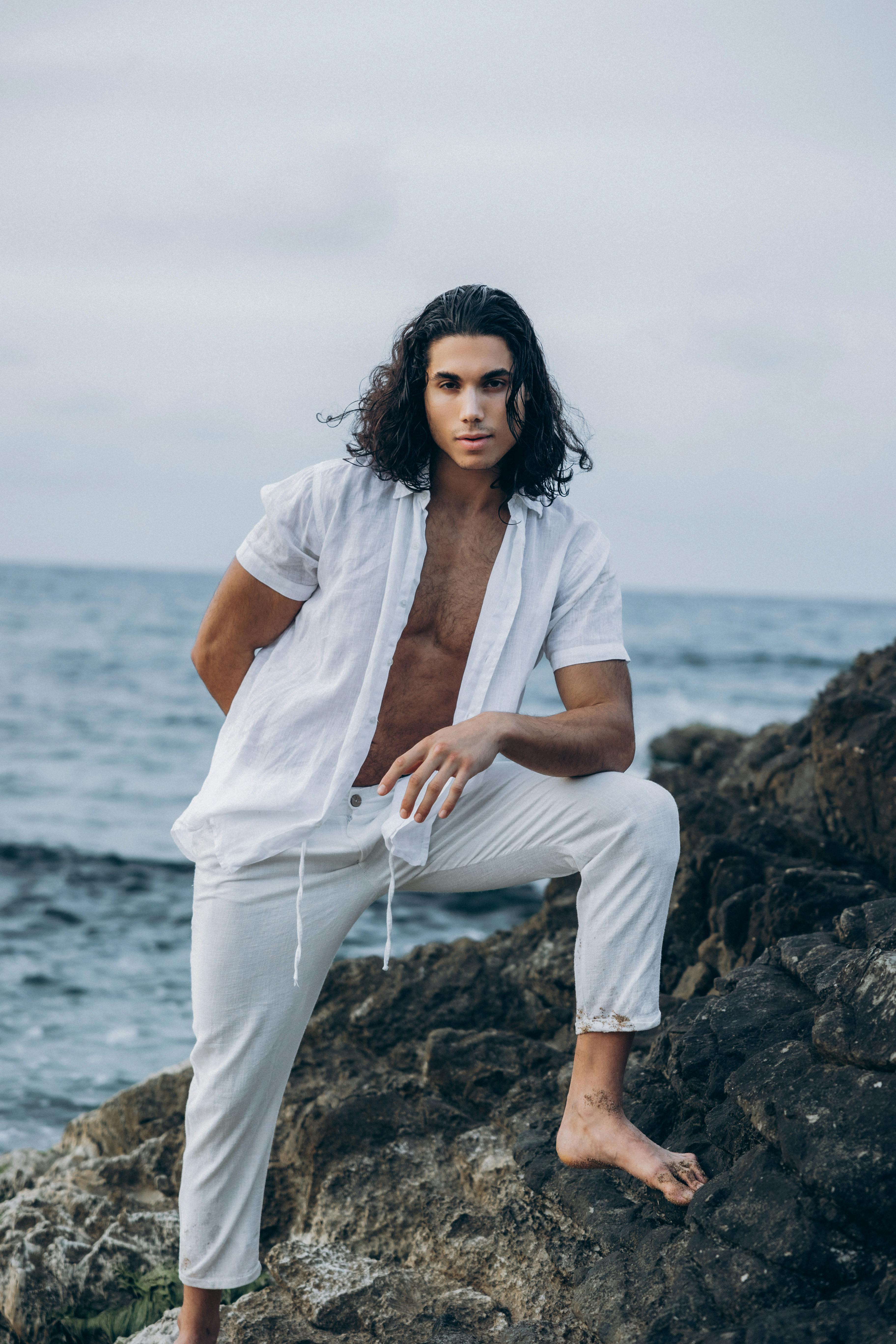 a man in white pants and shirt sitting on rocks