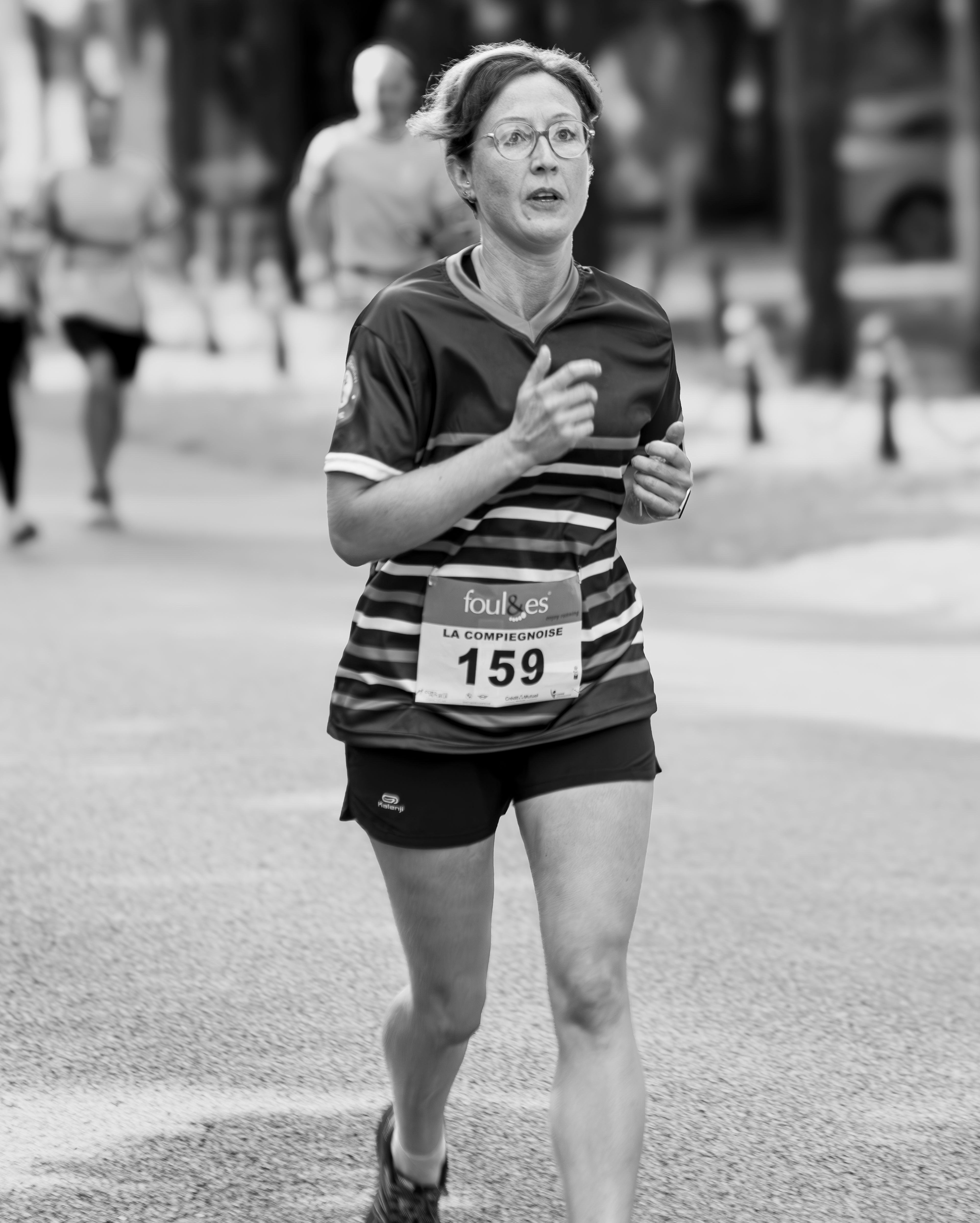 Focused woman running in an urban marathon, wearing sportswear and number tag.
