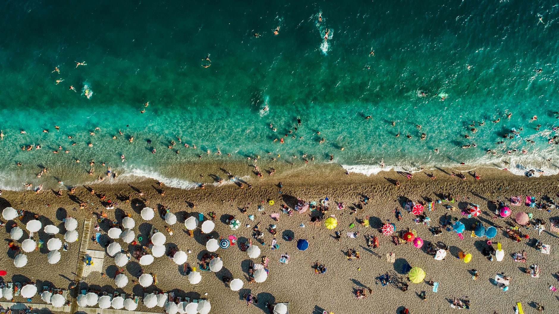 Vibrant summer scene on Antalya's Konyaalti Beach with turquoise waters and colorful umbrellas.