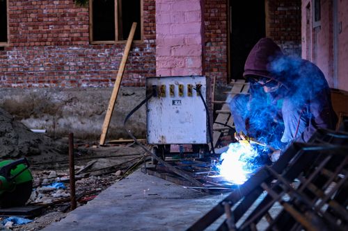 Free A welder in a hoodie works on metal in an urban setting, surrounded by blue sparks. Stock Photo