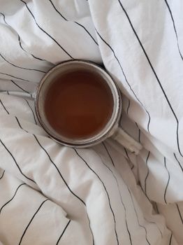 Top view of a cup of tea resting on striped bedclothes, exuding a cozy and refreshing vibe.