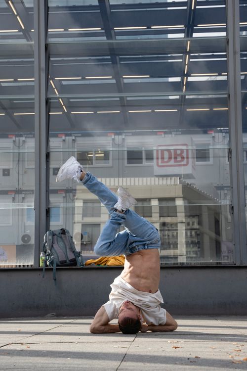 Free Breakdancer executing a headstand on a city pavement outside a building with glass windows. Stock Photo