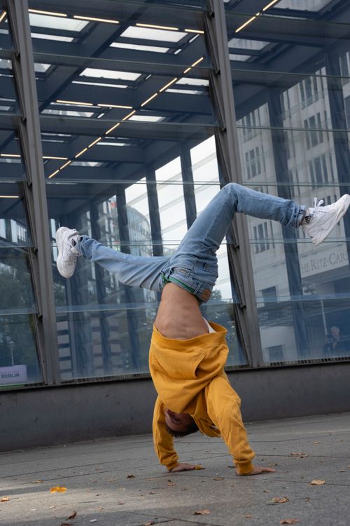 Free Man in yellow hoodie performing a handstand on city street against modern architecture. Stock Photo