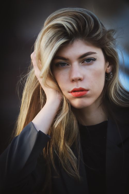 Free Close-up portrait of a young woman with striking blonde hair, wearing makeup, in an urban setting. Stock Photo