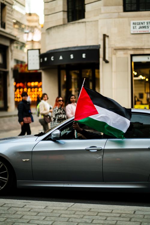 Free A car on city streets with a Palestinian flag held out, street scene background. Stock Photo