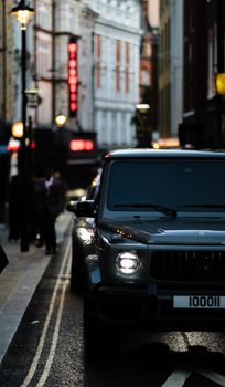 A luxury SUV with headlights on drives down a city street at dusk, highlighting urban life.