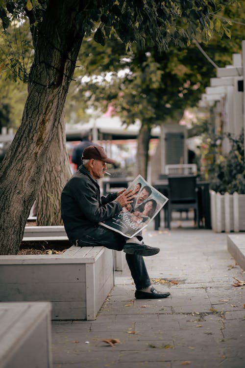 Old Man Reading Newspaper Smoking Cigarette on Bench 