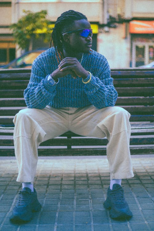 Young Man in Blue Sweater and White Pants Sitting on a Bench