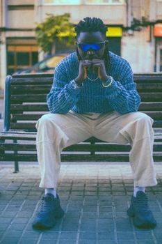 A fashionable man with sunglasses sitting on a city bench, showcasing a contemporary urban style.
