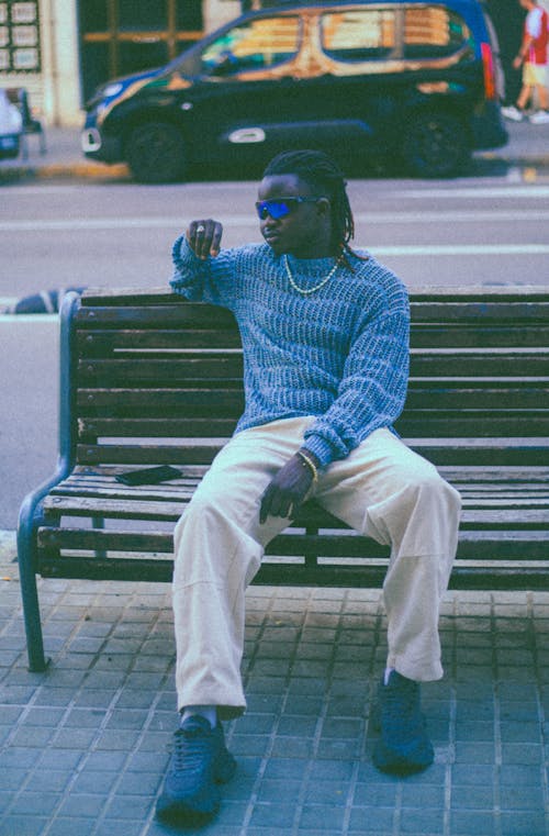 Man in Blue Sweater, White Pants, and Sunglasses Sitting on a Bench