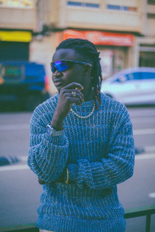 Musician in a Knitted Blue Sweater and Sunglasses Standing on Sidewalk