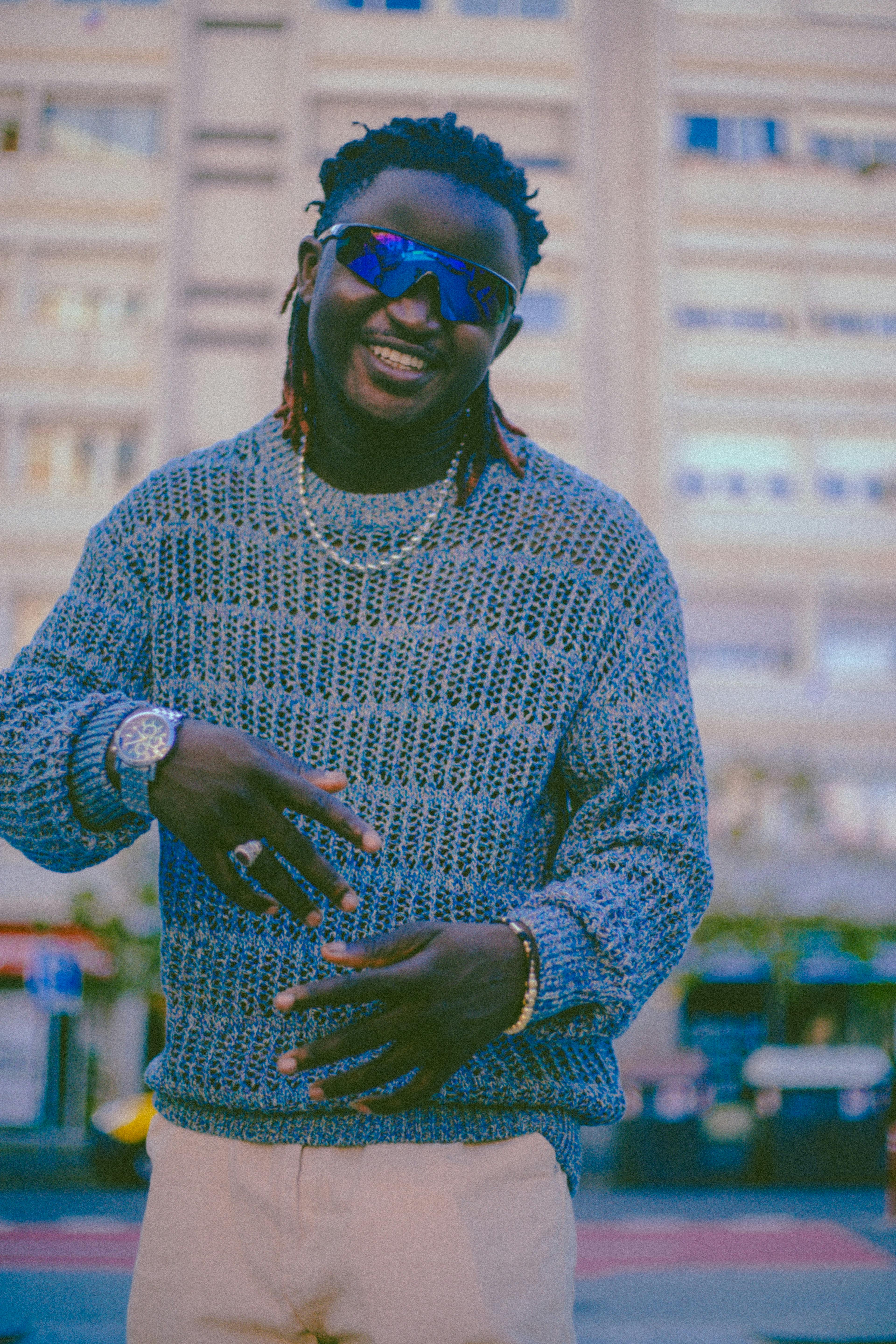 Fashionable man in a blue knitted sweater, smiling and posing outdoors with an urban backdrop.