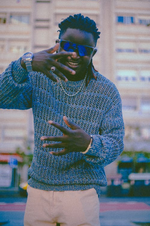 Gesticulating Musician in a Knitted Blue Sweater and Sunglasses on the Street