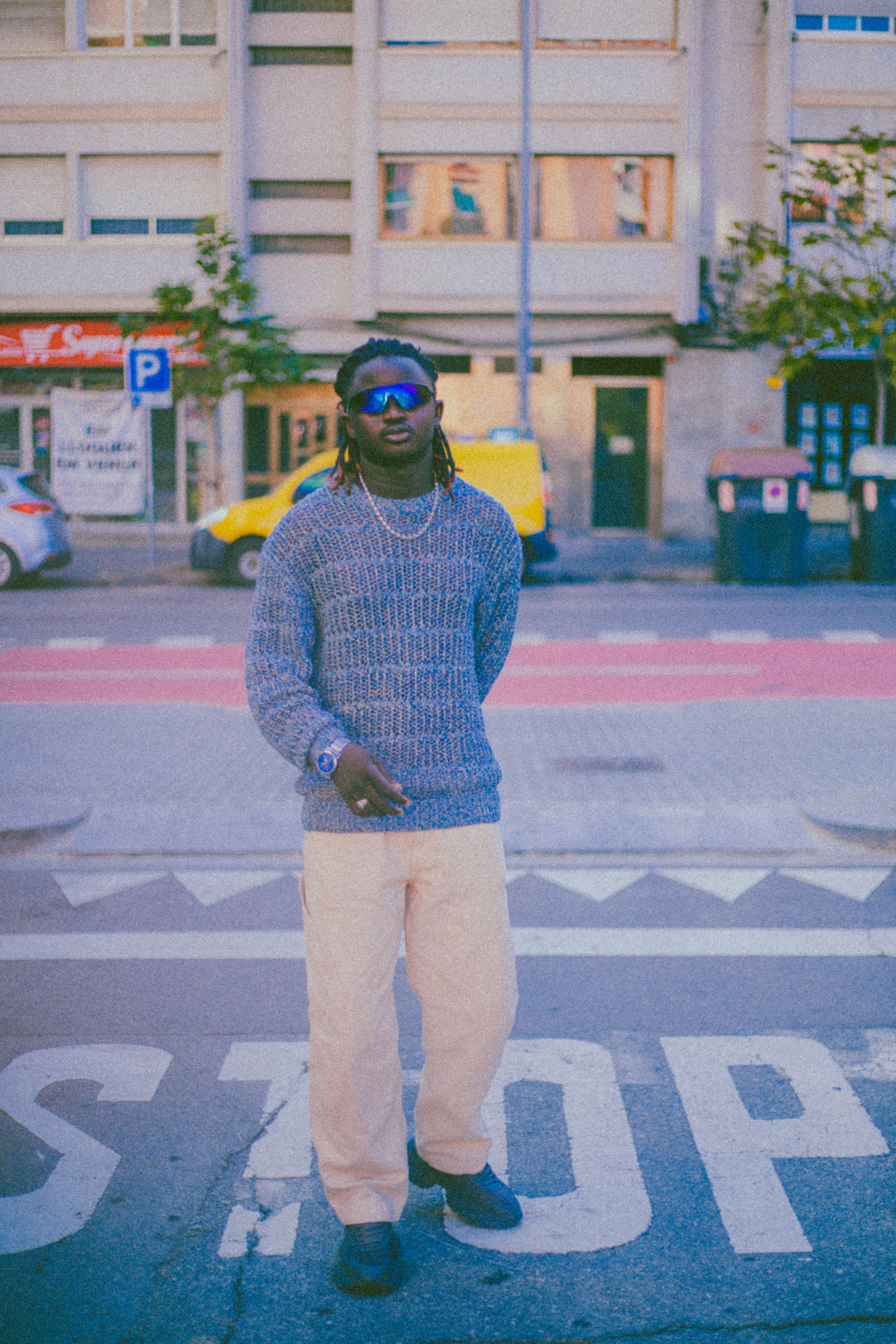 Stylish man in sweater and sunglasses poses boldly in an urban street setting.