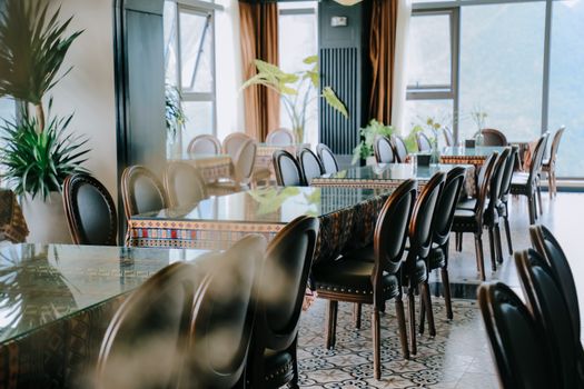 Chic restaurant featuring glass tables, elegant chairs, and lush plants in a bright modern interior.