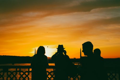 Free Silhouetted figures admire a vibrant sunset over a scenic bridge view. Stock Photo