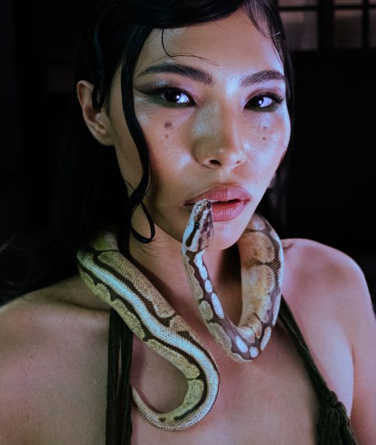 Close-up portrait of a woman with a snake elegantly draped around her neck, set against a dark background.