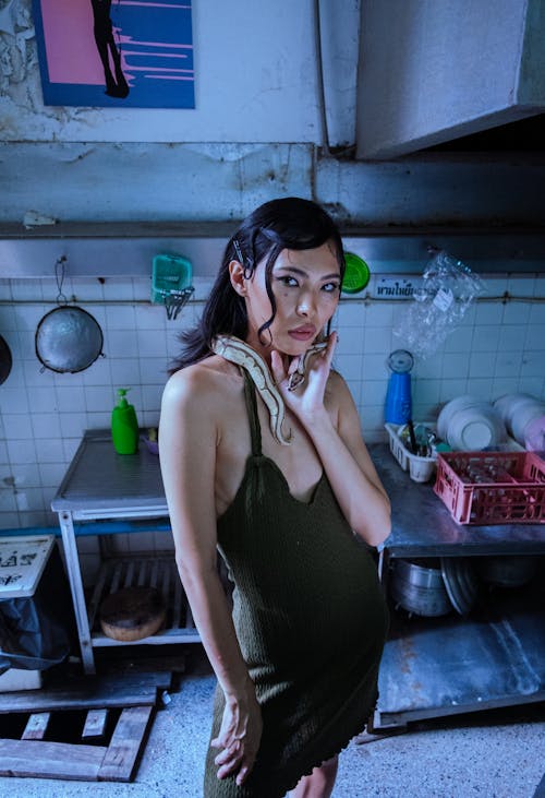 Woman in Black Dress and with Snake in Kitchen