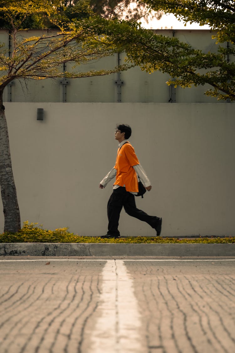 Young Man In Orange T-Shirt Walking On A Street