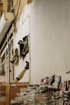 A city alley with mannequin legs on a wall and packaged goods on the ground.