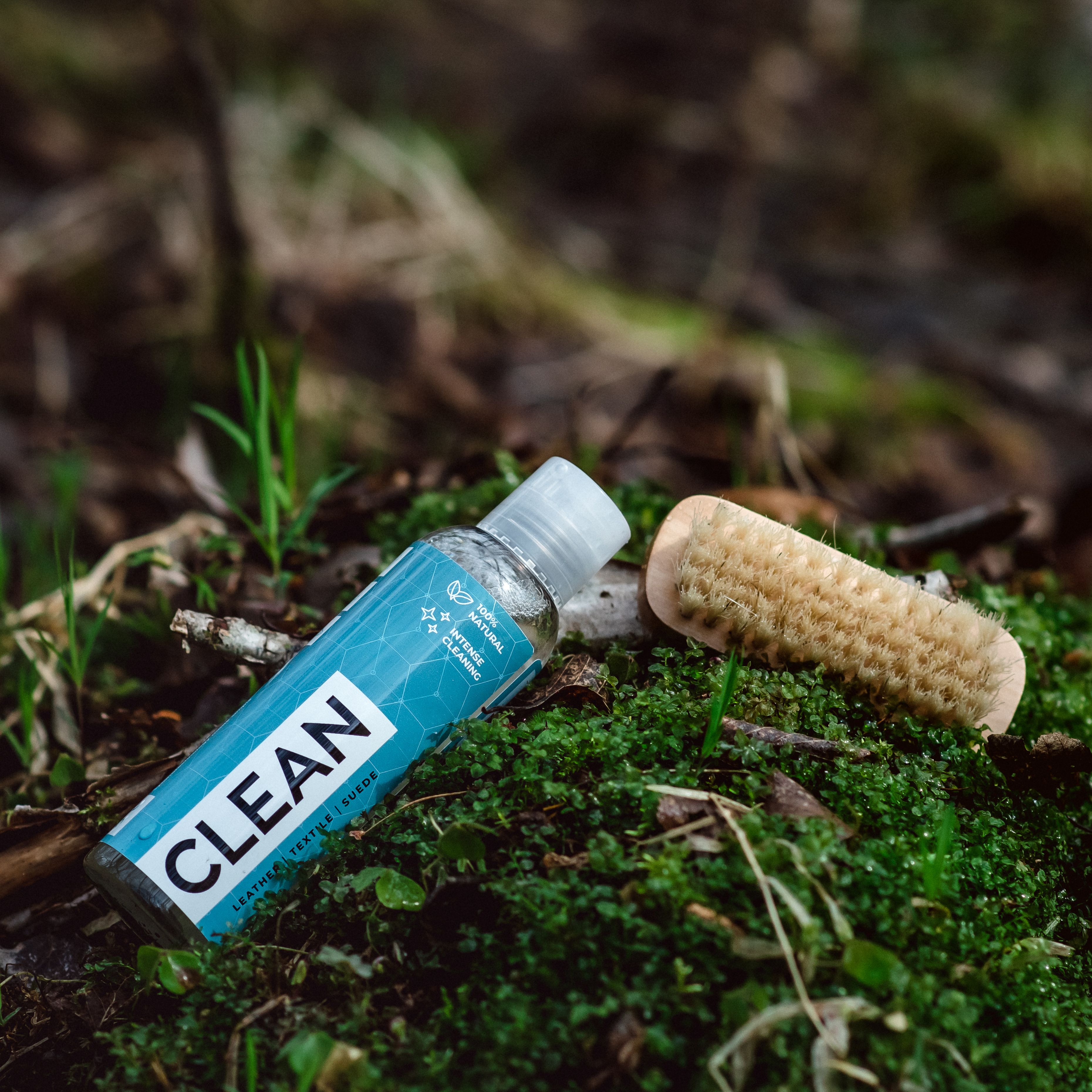 A bottle of eco-friendly cleaner and brush on lush forest moss, promoting natural cleaning methods.