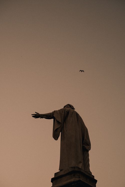 Free A powerful silhouette of a statue reaching outward against a dusky sky. Stock Photo