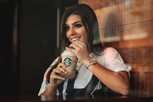 Young woman smiling while sipping a Starbucks iced coffee indoors.