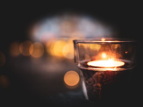 Free A glowing candle in a glass holder with a bokeh background, creating a cozy atmosphere. Stock Photo