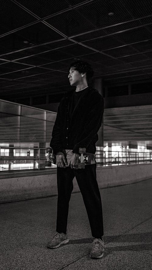 Black and White Photo of a Man Holding a Skateboard 