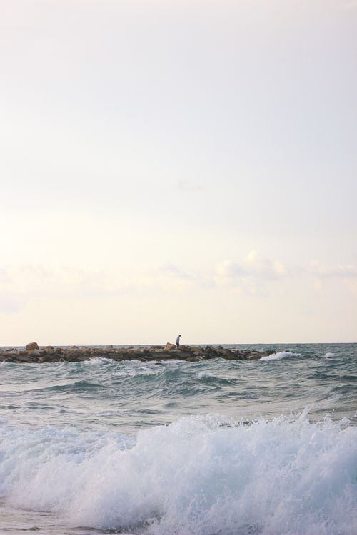 Free Calm ocean scene with waves crashing on a rocky breakwater under a pastel sky. Stock Photo