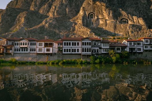 Charming Ottoman-style houses line the riverside under a rocky backdrop in Amasya, Türkiye.