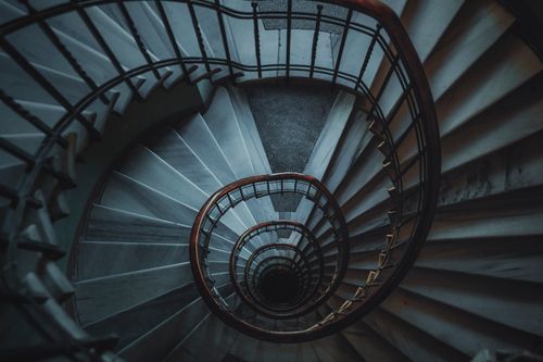 Free A dark, moody aerial view of a spiral staircase with wooden handrails. Stock Photo