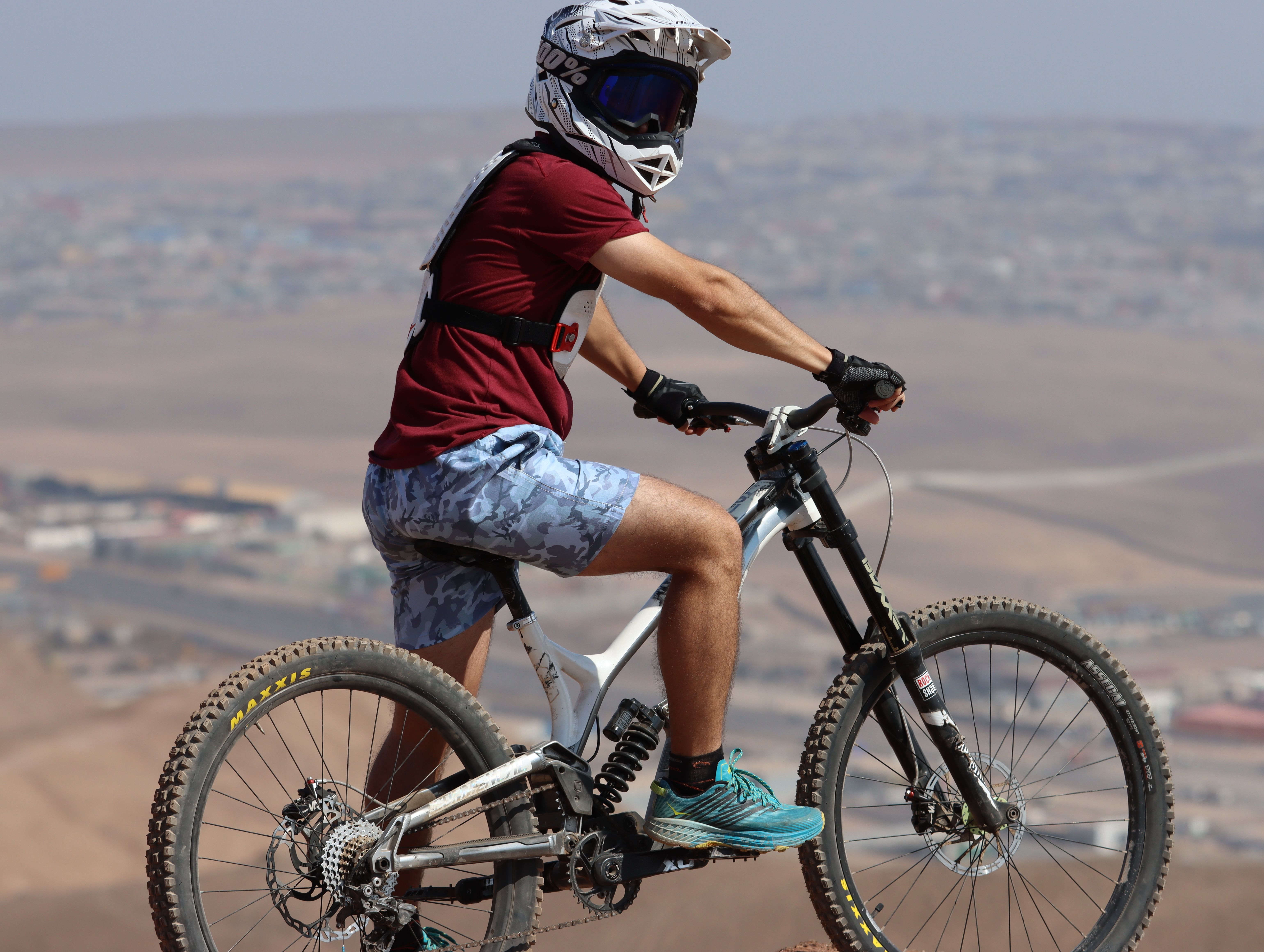 Man wearing helmet and goggles rides a mountain bike in a desert area, showcasing adventure and sportsmanship.