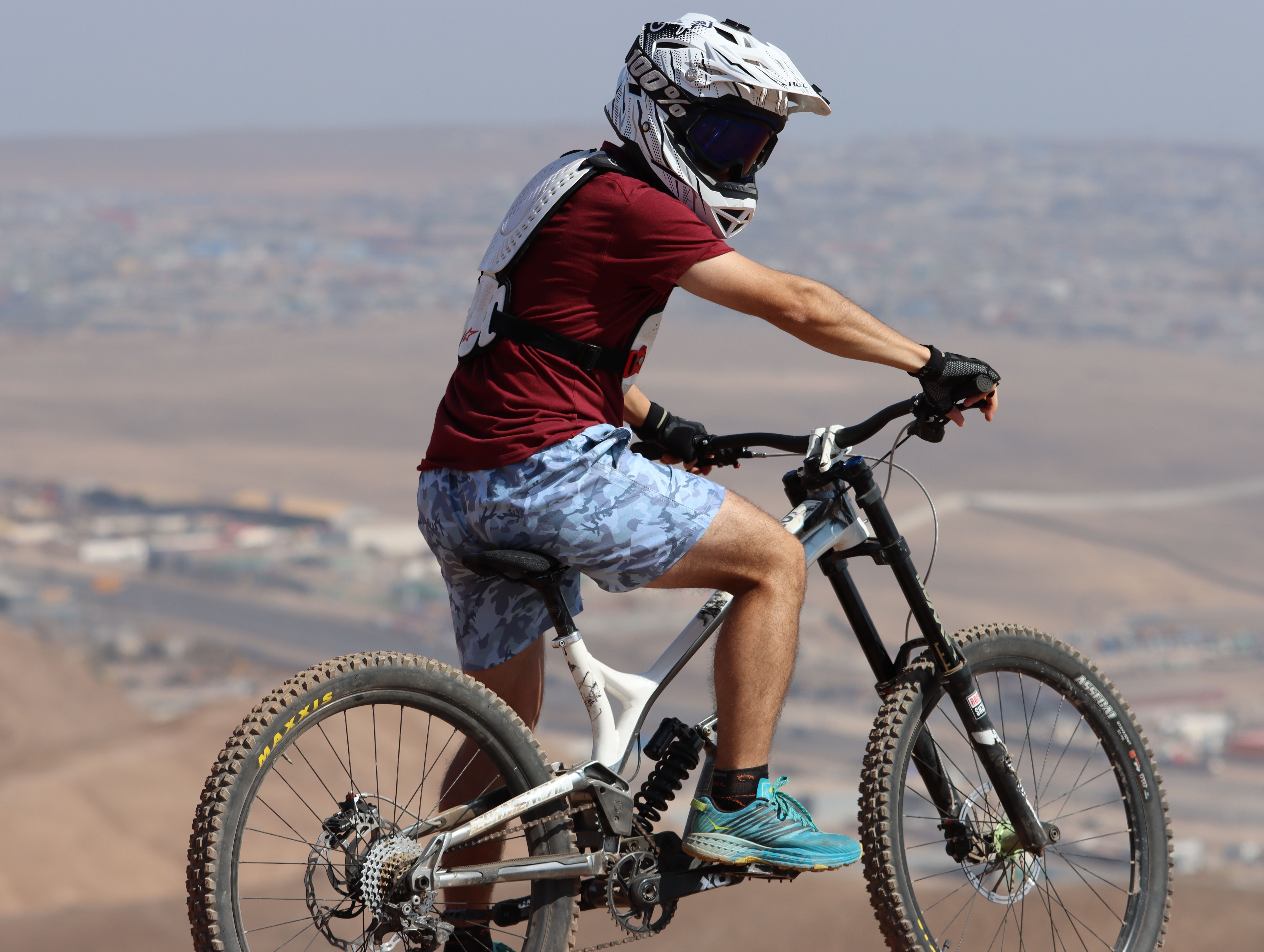 A cyclist rides a mountain bike through arid desert landscape, wearing a helmet and goggles.