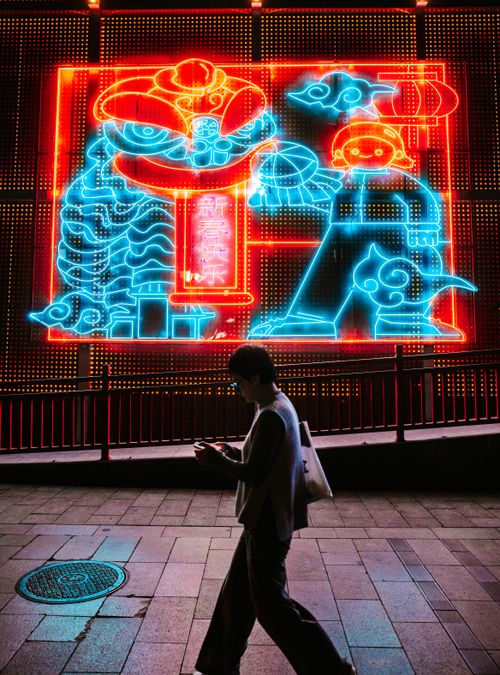 Free Anonymous woman walks past vibrant neon wall art at night, her silhouette illuminated by colorful lights. Stock Photo