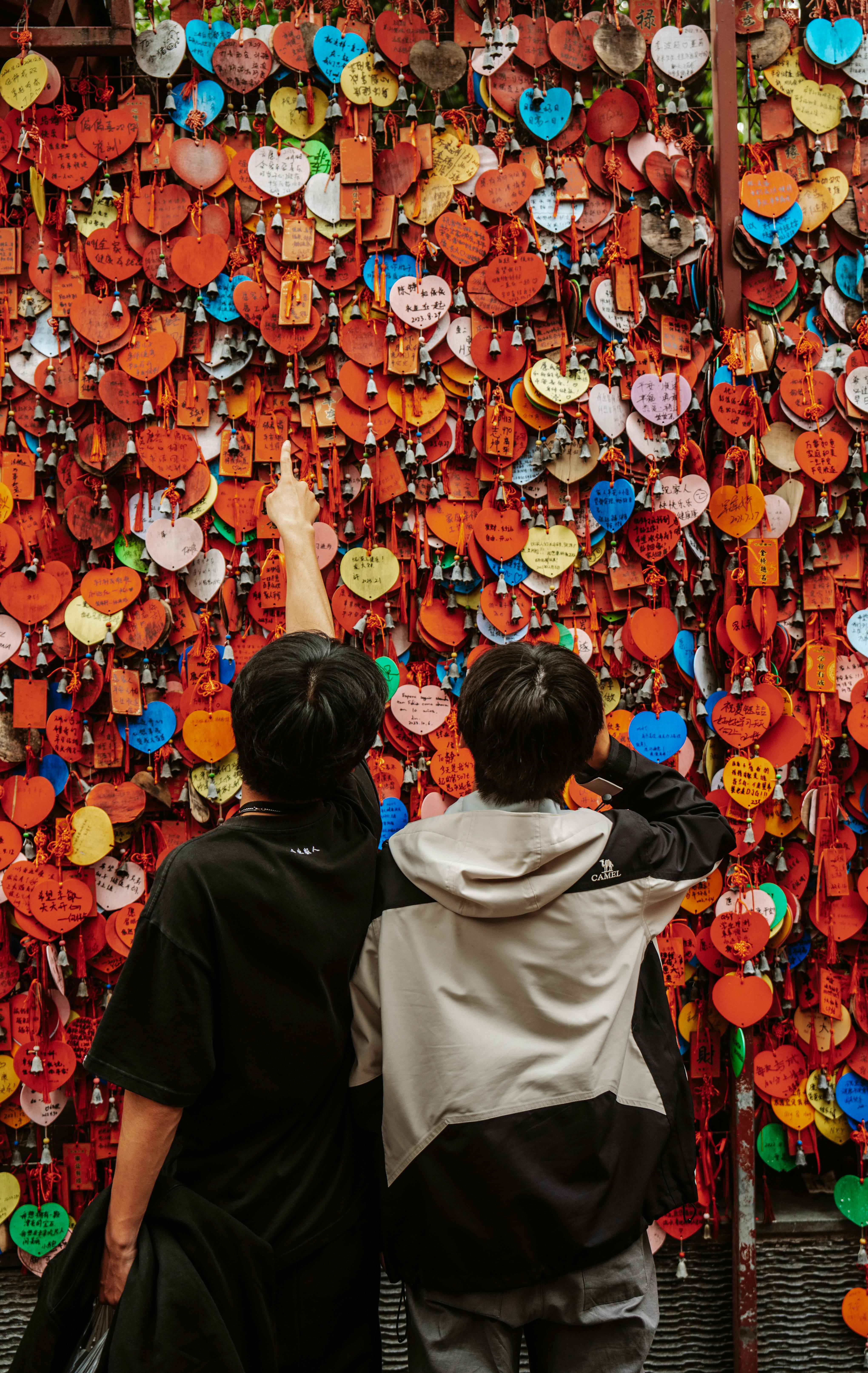 Two individuals in casual attire looking at a vibrant wall of heart-shaped notes symbolizing love and wishes.