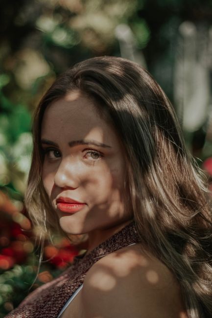 A young woman posing outdoors with sunlight creating artistic shadows on her face.