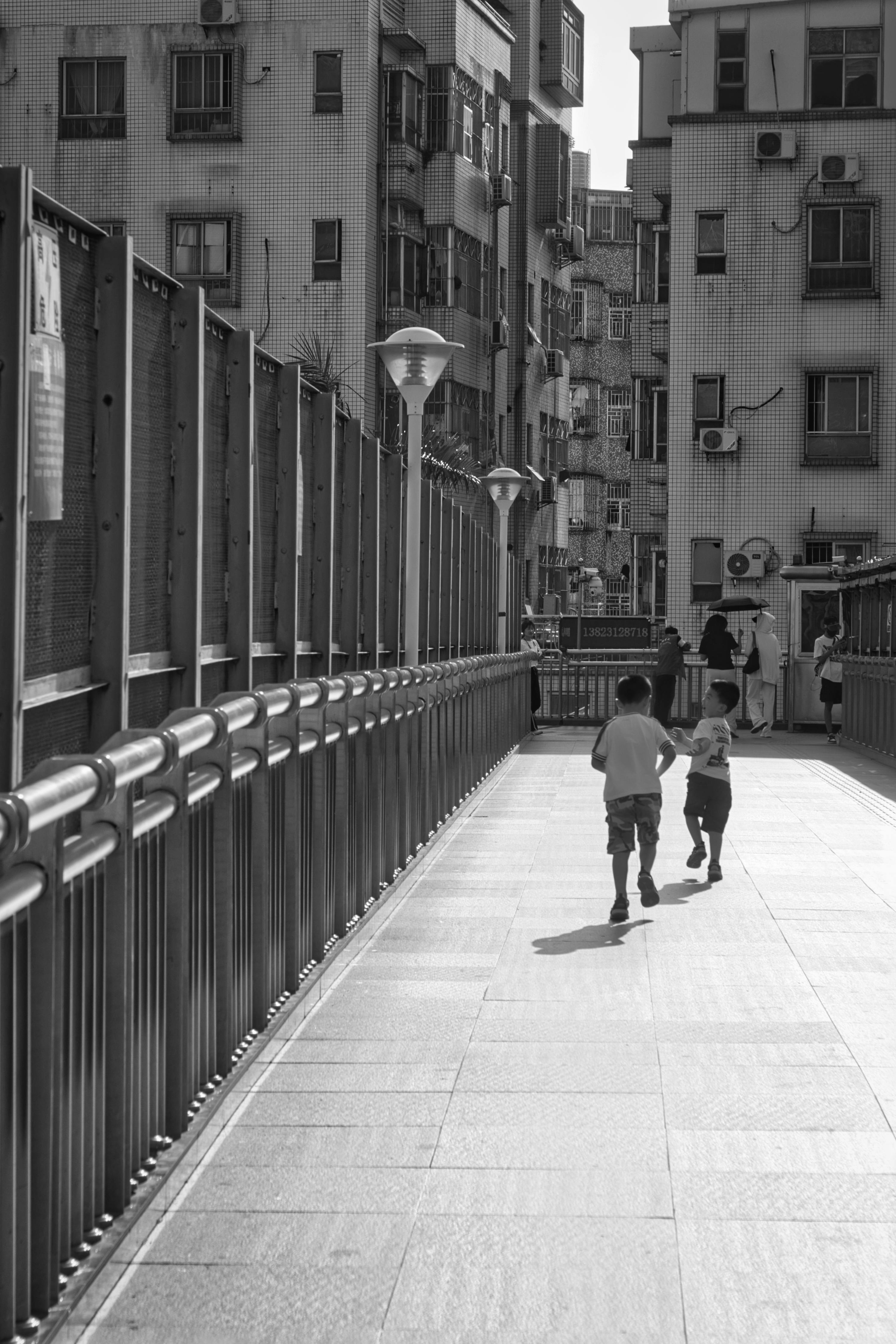 Black and white photo of children running on a city bridge, capturing urban childhood joy.