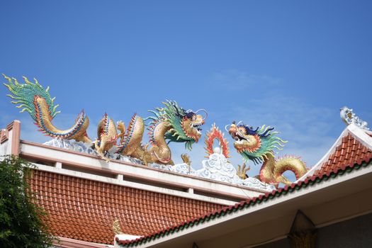 Colorful dragon sculptures adorn the roof of a Thai temple under a clear blue sky.