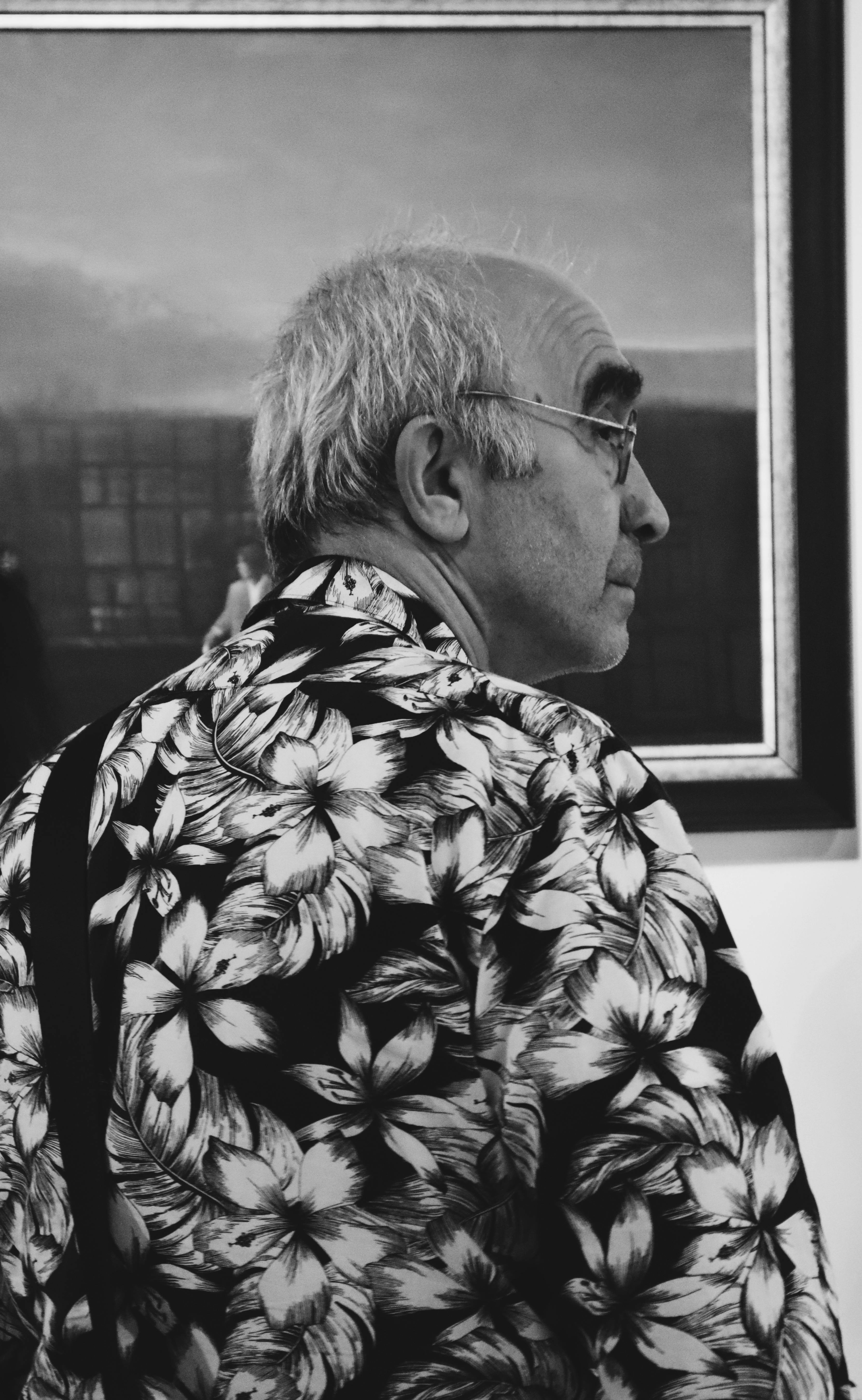 An elderly man with a floral shirt observing art in a gallery.