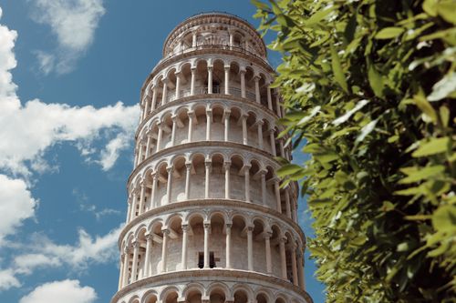 Free Stunning view of the Leaning Tower of Pisa with lush greenery and blue sky. Stock Photo