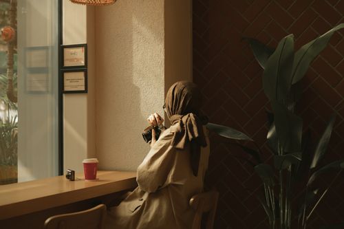 Free A woman in a hijab enjoys coffee while holding a camera in a cozy café setting. Stock Photo