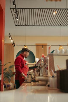 A barista wearing a red apron making coffee in a stylish café with contemporary decor.
