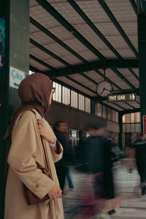 Free A woman in a hijab stands at a lively train station platform surrounded by moving pedestrians. Stock Photo