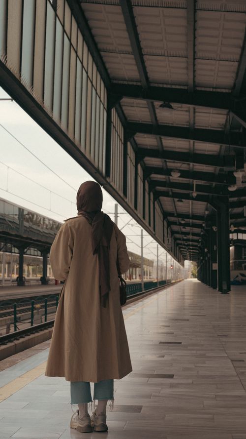 Free A woman in a hijab stands on an empty railway platform in an urban setting. Stock Photo