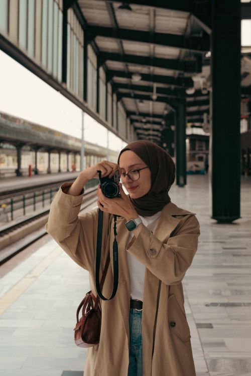 Free A woman in a hijab takes photos with a camera at an urban railway platform. Stock Photo
