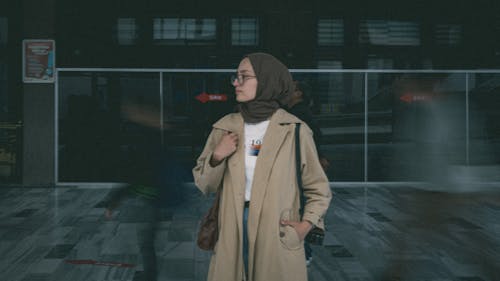 Woman in a Trench Coat Standing among People Walking in the Hallway 