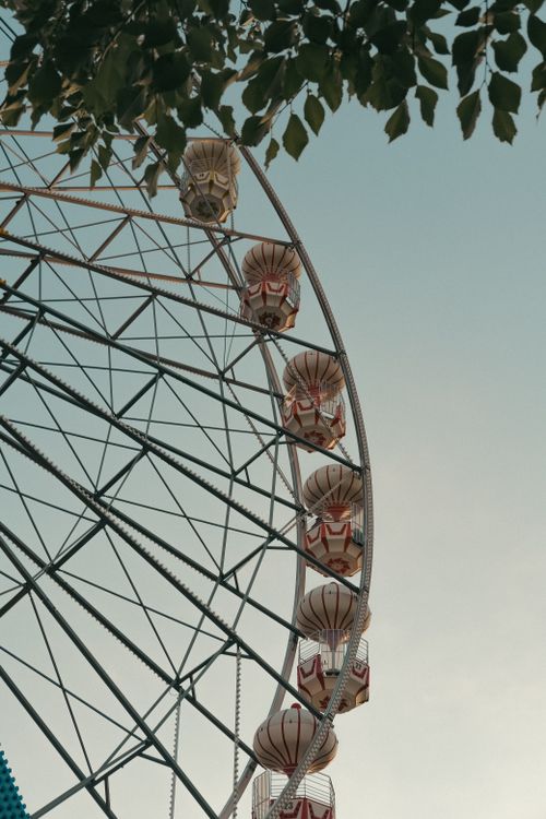 Free Low angle shot of a ferris wheel under a clear blue sky with visible leaves. Stock Photo
