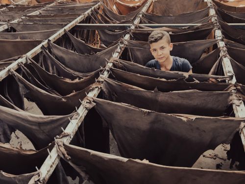 Free Young boy in a tannery standing among rows of drying leather hides, showcasing traditional leather production. Stock Photo
